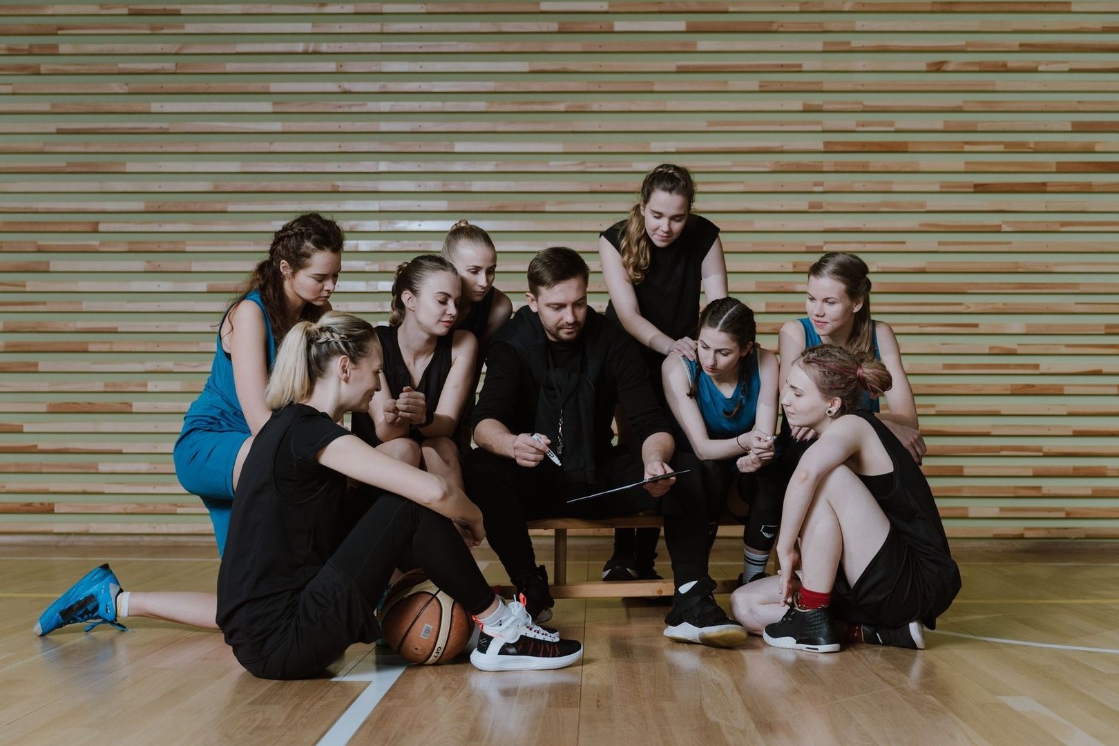 Sportgruppe bespricht sich mit Trainer und Unterlagen in einer Turnhalle