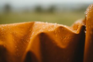 Nahaufnahme einer orangefarbenen Jacke mit abperlenden Wassertropfen