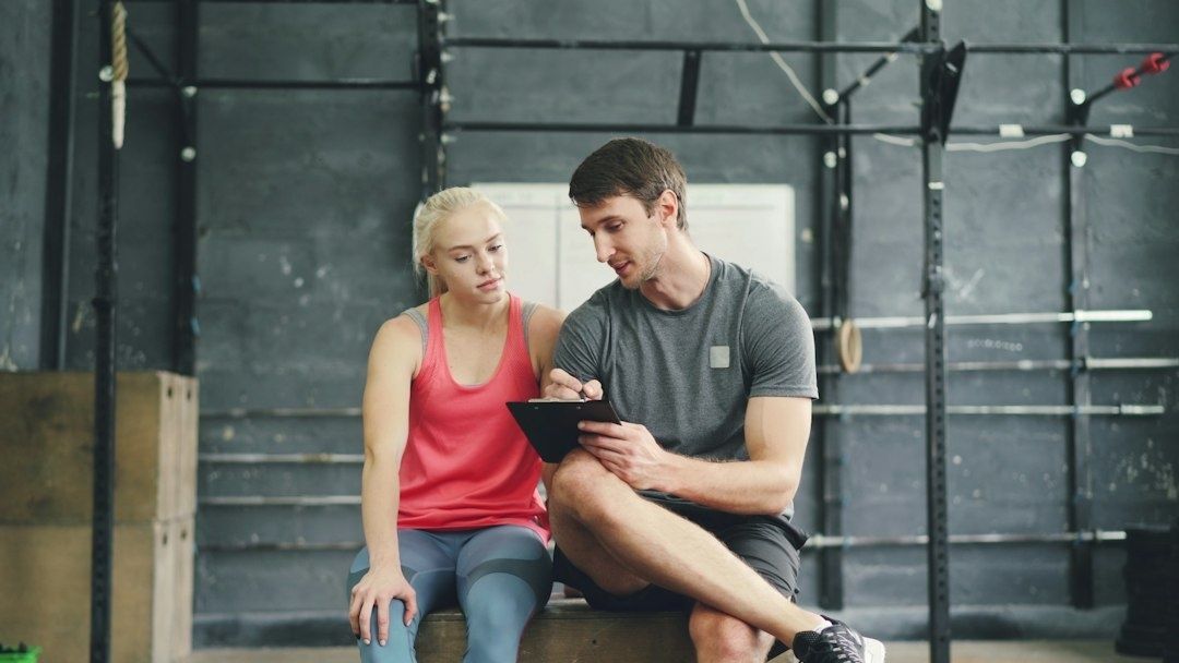 Trainer und Sportlerin besprechen Trainingsdaten auf einem Tablet im Fitnessstudio
