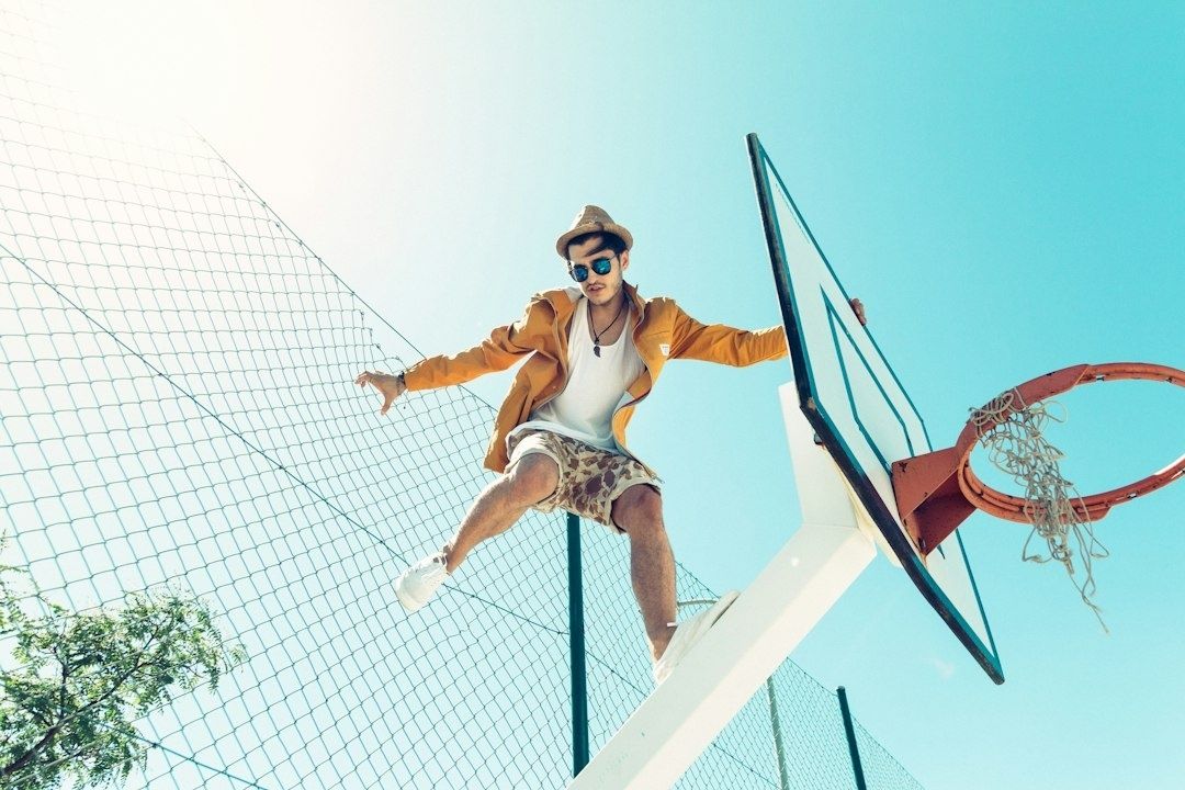 Basketballspieler mit Sonnenbrille springt neben einem Basketballkorb
